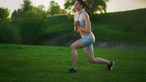 A-close-up-of-a-young-woman-performs-alternate-lunges-on-each-leg-in-the-jump.-Jump-out-in-the-park-at-sunset